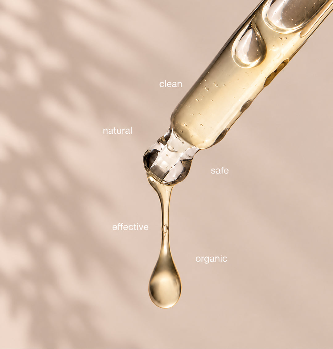 A golden hair oil dripping from a glass dropper, labeled clean, natural, safe, effective and organic.