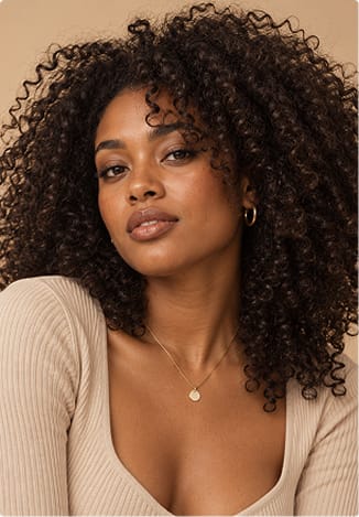 A woman with voluminous, defined dark curls against a warm beige background.