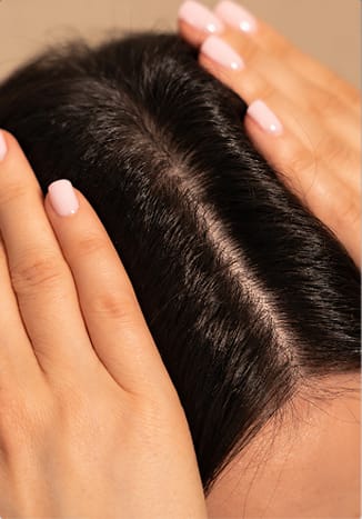 A close-up of hands parting dark hair to show a healthy scalp.