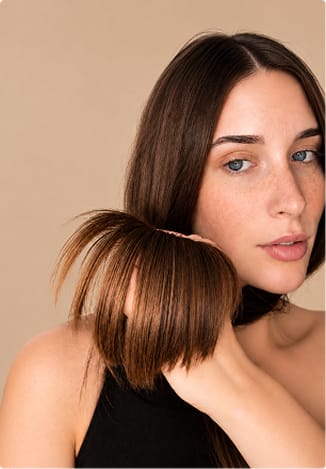 A woman holding up the dry, split ends of her straight brown hair.