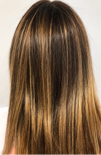 The back of a woman's head after treatment, showing smooth, shiny, highlighted brown hair. after